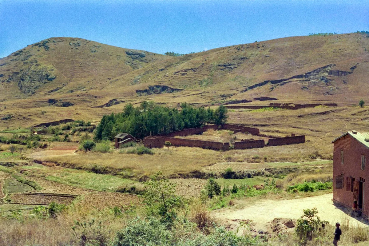 A hamlet of red-earth houses and a walled compound in a valley of terraced fields, bare highland hills rising behind it